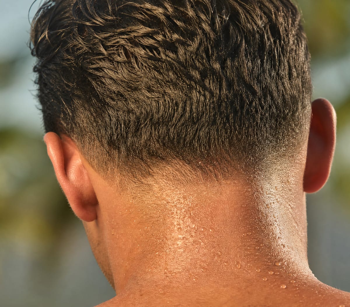 Nuca masculina com gotas de suor em dia quente, sob vegetação tropical